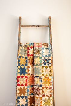 an old ladder is holding a quilt on it's side and hanging from the wall