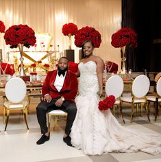 a bride and groom sitting at a table with red flowers