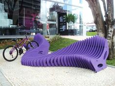 a purple bench sitting on top of a sidewalk next to a bike