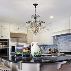 a chandelier hanging from the ceiling in a kitchen with marble counter tops and white cabinets