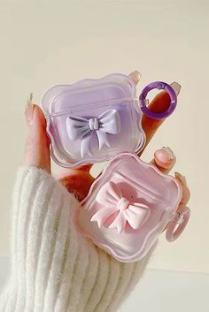 a person holding three small cases with bows on them, one in pink and the other in purple