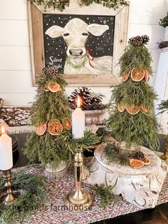 a table with candles and christmas decorations on it, in front of a cow painting