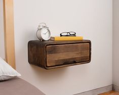 an alarm clock and some books on a shelf next to a bed with eyeglasses