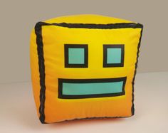 a yellow square pillow with blue eyes and black trim on the front, sitting on a white surface