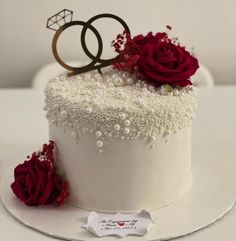 a wedding cake with white frosting and red roses on the top is decorated with pearls