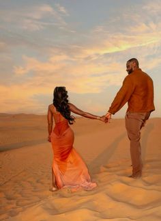 a man and woman holding hands in the sand dunes at sunset or sunrise, with clouds in the sky