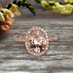 an oval shaped morganite and diamond ring on a wooden table with flowers in the background