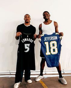 two men holding up jerseys in front of a white wall