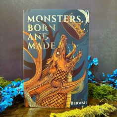 a book sitting on top of a wooden table next to blue and green flowers with the title monsters born and made