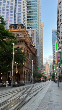 an empty city street lined with tall buildings and green traffic lights in the middle of the day