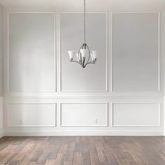 an empty room with white walls and wood flooring is pictured in this image, there are two chandeliers hanging from the ceiling