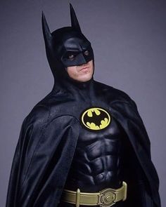 a man dressed as batman standing in front of a gray background