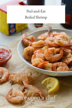 a bowl filled with cooked shrimp next to lemon wedges and ketchup sauce