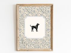 a black dog standing in front of a white wall with leaves on it's frame