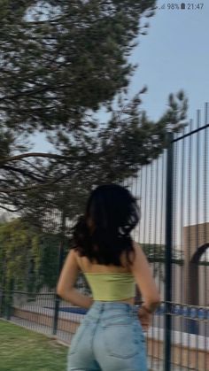 a woman standing in front of a fence with her back to the camera, wearing high waist jeans