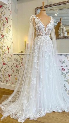 a white wedding dress on display in front of a wallpapered room with candles