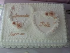 two heart shaped cakes with roses on them are sitting on a purple tablecloth, and the cake is decorated in white frosting