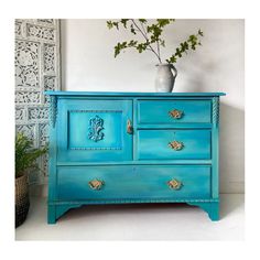 a blue dresser with gold handles and knobs on the doors is next to a potted plant