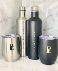 three stainless steel wine bottles and two tumblers sitting on a marble countertop next to each other