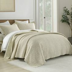 a bed with white sheets and pillows next to a potted plant on the floor