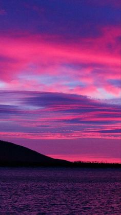 the sky is pink and purple as it sits on top of a hill over water