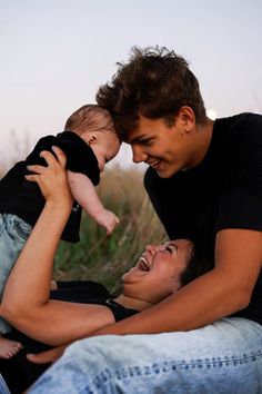 a man holding a baby in his arms while sitting next to another man on the ground