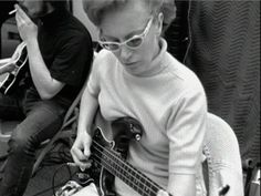 black and white photograph of a woman playing an electric bass guitar while another person sits in the background