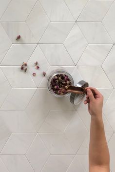 a person is pouring something into a bowl on the floor in front of a white tiled wall