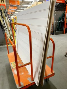 an orange hand truck with a surfboard on it's back in a store