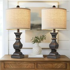 two lamps sitting on top of a wooden dresser next to a vase with a plant in it