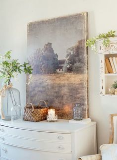 a white dresser topped with a vase filled with flowers next to a painting on the wall