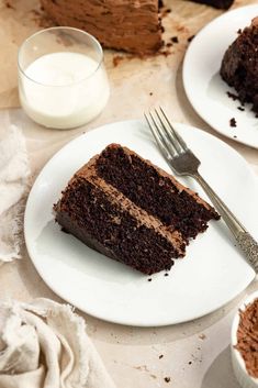 two slices of chocolate cake on white plates next to a glass of milk and fork