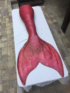 a large red mermaid tail laying on top of a white tablecloth covered bed in a room