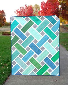 a blue and green quilt sitting on the side of a sidewalk in front of trees