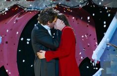 a man and woman are kissing in front of a stage backdrop with confetti