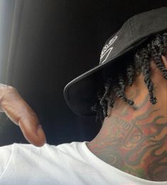 a man with dreadlocks and a baseball cap pointing at something in the distance