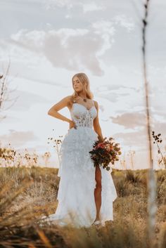 a woman in a white wedding dress standing in a field with her hands on her hips