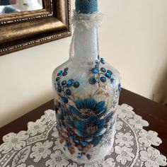 a glass bottle with blue flowers on it sitting on a doily next to a mirror