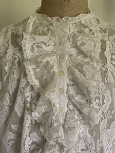 A lovely vintage blouse in a floral lace with frills at either side of the button placket. It has three darts at each shoulder and darts at the front and back waist . The sleeves are 3/4 in length and have a generous sleeve head kept in shape by an inner fabric frill . The cuffs are shaped and have a small lace frill where they join the sleeve. The blouse is in great condition and has one almost invisible mend as shown in the images.  It looks wonderful under a black jacket which is also shown i Classic Lace Tops With Lace Work, Classic Lace Tops For Daywear, Lace Top With Ruffles For Daywear, Classic Lace Blouse, Daywear Scalloped Lace Fitted Tops, Fitted Scalloped Lace Tops For Daywear, Classic Lace Tops For Wedding, Vintage Lace Trim Tops In Antique White, Vintage White Lace Trim Tops