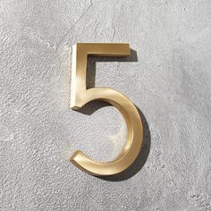 the number five is shown in gold on a white wall with grey concrete flooring