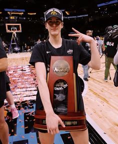 a woman in black shirt holding up a trophy on top of a basketball court with confetti all around her