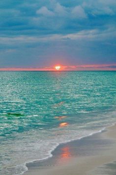 the sun is setting over the ocean with clouds in the sky and water on the beach