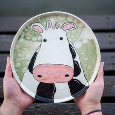 a hand holding a plate with a painting of a cow on it's face