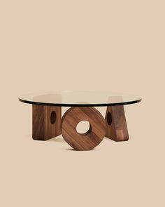 an oval glass table with wooden legs and a circular design on the top, against a beige background