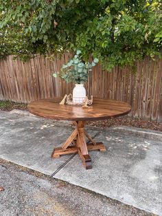 a wooden table sitting on top of a cement floor next to a green bush and fence