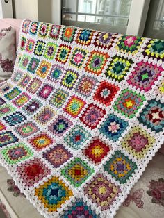 a crocheted granny blanket is displayed on a bed in a room with windows