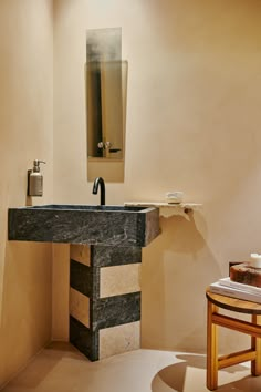 a bathroom sink sitting under a mirror next to a wooden stool and table with soap dispenser on it