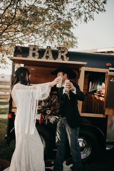 a man and woman standing in front of a food truck drinking wine from their glasses