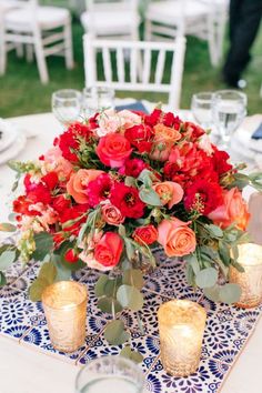 a bouquet of red roses and greenery sits on a table with gold votives