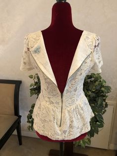 This is a lovely Hearts Brand Blouse. It has a rounded neck line, short sleeves, and decorative lace all over. The shell is made of 56% cotton and 44% nylon. The inside lining is made of 100% cotton. It is recommended to hand wash in cold water and line dry. Do not bleach or Dry Clean. Use a low iron. The Blouse has a zipper closure in back and a lovely fitted waist. It is a cream/off white color. It is a size Medium with the following measurements: 32” Bust 28” Waist 20.5” Length 7.5” Sleeves T Summer Lace Patchwork Short Sleeve Top, Short Sleeve Lace Top With Ruffles, Short Sleeve Lace Tops With Ruffles, Lace Ruffle Tops With Short Sleeves, Lace Tops With Ruffles And Short Sleeves, Fitted V-neck Top With Scalloped Lace, Lace Top With Ruffles And Short Sleeves, Chic Short Sleeve Blouse With Lace Patchwork, Fitted Short Sleeve Lace Top With Ruffles